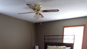 Une chambre à coucher avec un lit, une table de chevet, une lampe et un ventilateur de plafond.