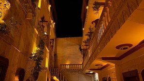 Un pasillo ornamentado y tenuemente iluminado, con una fuente circular en el centro, flanqueado por balcones con plantas en macetas.