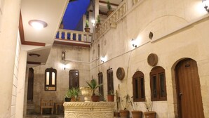 Un patio con una fuente central, plantas en macetas y puertas de madera.