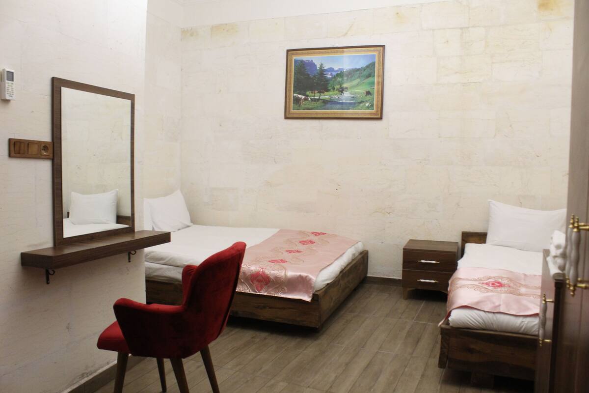 A bedroom with two beds, a red chair, a wooden nightstand, a bedside table, a mirror, and a framed picture on the wall.
