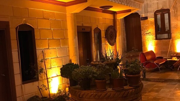 Un patio con paredes de piedra, una jardinera central con plantas en macetas y una puerta de madera.