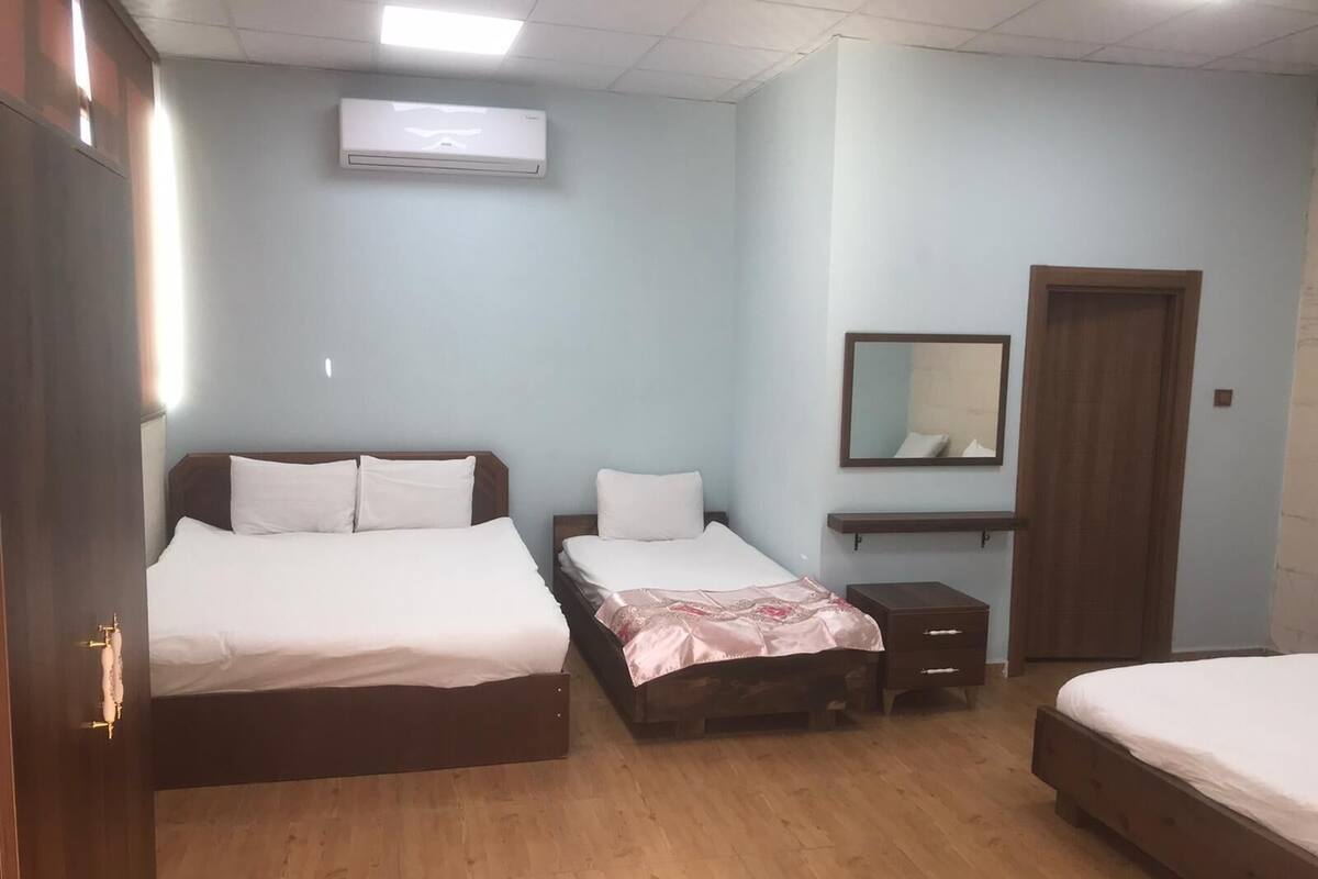 A hotel room with two beds, a wooden floor, a mirror, and a small bedside table.