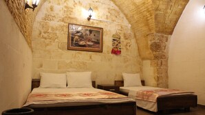 Una habitación con dos camas de madera, una pared de piedra, un cuadro enmarcado y un adorno colgante.
