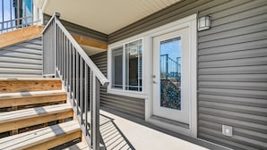 A wooden deck with a metal railing, a door with a glass panel, and a window with a view of a bridge.