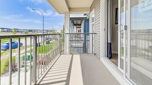 A balcony with a metal railing, a glass door, and a view of a parking lot and buildings in the distance.