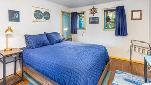 Ein Schlafzimmer mit einem großen Bett, einem Nachttisch, einer Lampe, einem Fenster mit Vorhängen, einer Wanduhr und gerahmten Bildern.