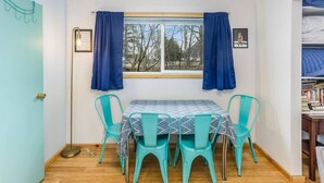 Ein Zimmer mit Tisch, vier Stühlen, einem fenster mit Vorhängen, einer Tür und einem Bücherregal mit Büchern.