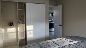 Un dormitorio con cama, armario y una kitchenette al fondo.