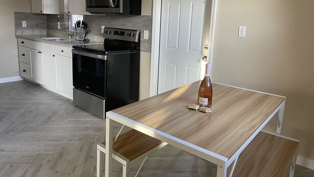 Una cocina moderna con microondas integrado, horno y fregadero. Hay una mesa de madera con una botella de vino y un abrelatas.