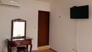 A room with a wooden dresser, a mirror, a television mounted on the wall, and a door. - San Román room inside the historic center (Campeche)