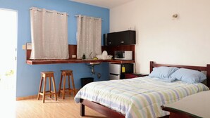 A bedroom with a bed, a wooden headboard, a nightstand, a TV, a microwave, a sink, and two stools. - San Román room inside the historic center (Campeche)