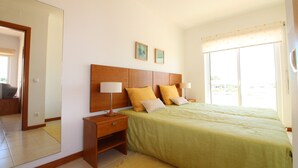 A bedroom with a large bed, two bedside tables with lamps, a mirror, and two framed pictures on the wall. - Falésia Beach - Wifi, Piscina e Varanda (Albufeira)