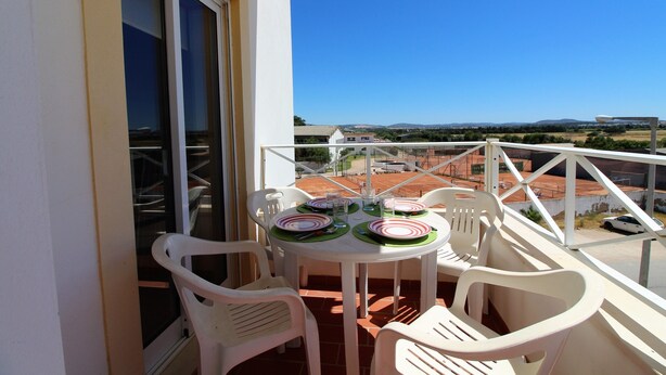 A balcony with a table set for four, white plastic chairs, and a clear view of the surrounding landscape. - Falésia Beach - Wifi, Piscina e Varanda (Albufeira)