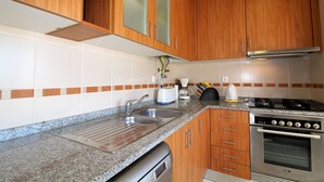 A kitchen with wooden cabinets, a stainless steel sink, a built-in oven, and a coffee maker. - Falésia Beach - Wifi, Piscina e Varanda (Albufeira)