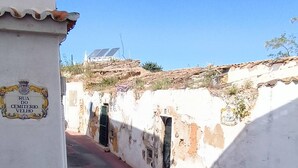 Une rue étroite avec un bâtiment blanc portant l’inscription « Rua do Cemitério Velho » et un lampadaire.
