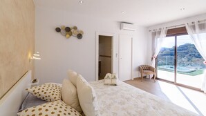 A bedroom with a bed, pillows, a chair, and a view of a pool and hills. - El Refugio de Árchez by Ruralidays (Málaga)