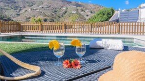 A poolside setting with two glasses of a clear beverage, a towel, and a wicker chair. - El Refugio de Árchez by Ruralidays (Málaga)