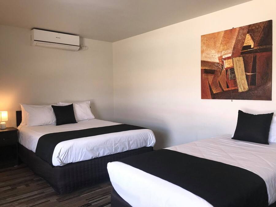 Ein Hotelzimmer mit zwei Betten, einer Wand-Klimaanlage und einem großen abstrakten Gemälde.