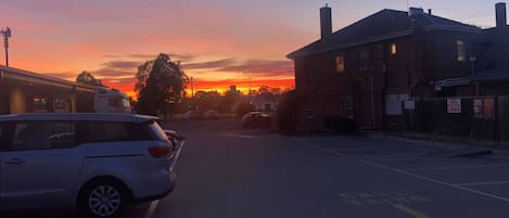 Une rue au coucher du soleil, avec une voiture blanche garée sur le bord.