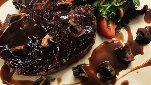 Un plato con un bistec, champiñones y una ensalada.
