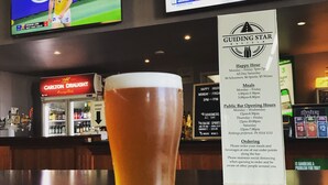 Zona de bar con una cerveza en un vaso, una pantalla de deportes y un tablero de menú.