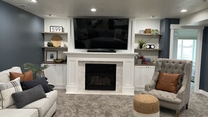 Uma sala de estar com lareira, televisão e uma poltrona cinza.