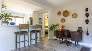 Een keuken met houten barkrukken, een eettafel met stoelen, een klein bureau en decoratieve wandkunst.