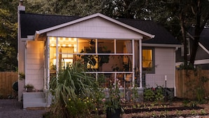 Een huis met een groot raam, een houten omheining en een tuin vol planten en bloemen.