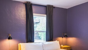 A bedroom with a wooden bed, two bedside tables, a window with curtains, and a wall-mounted light fixture.