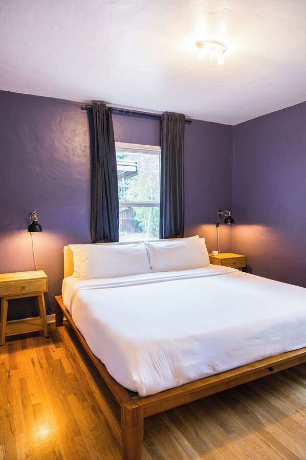Een slaapkamer met een houten bed, twee nachtkastjes, een raam met gordijnen en een wandlamp.