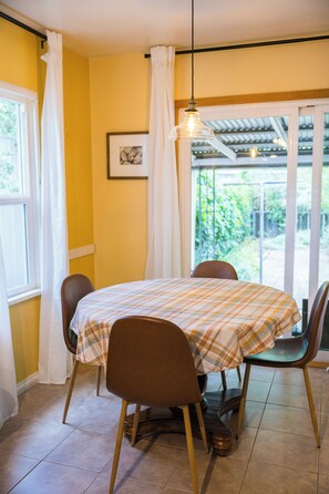 A dining area with a table and chairs, a hanging light fixture, a window with curtains, and a framed picture on the wall.
