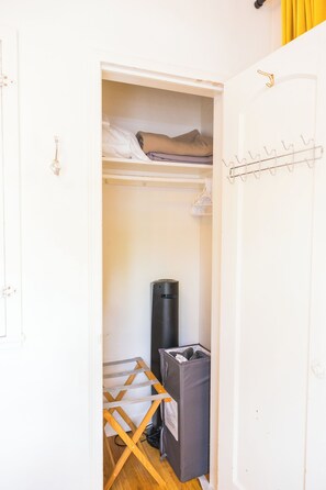 A narrow walk-in closet with a hanging rod, a drying rack, and a trash bin.