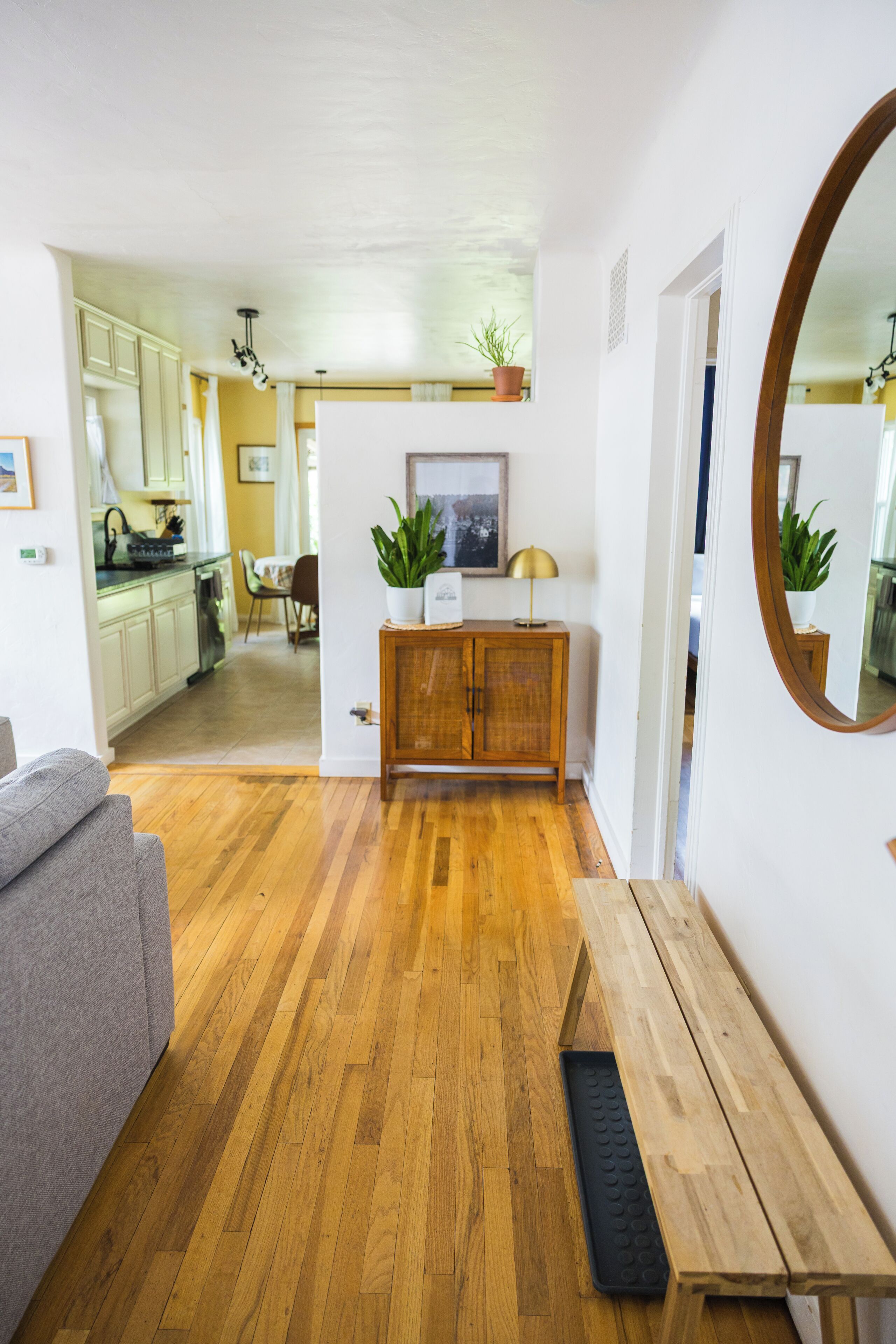 A modern living room with hardwood flooring, a grey sofa, a wooden side table, and a mirror.