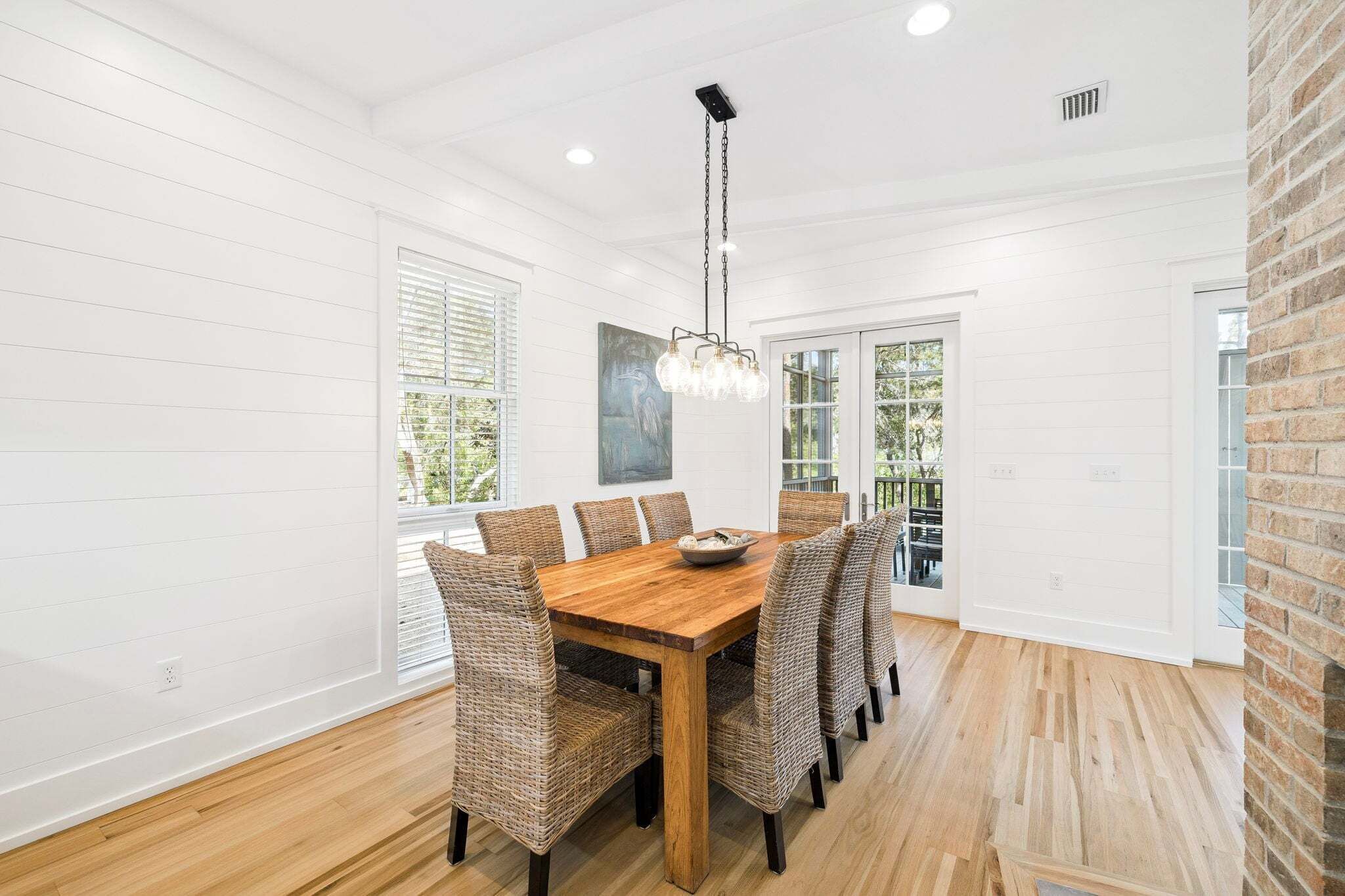 A dining room with a wooden table and wicker chairs, white walls, and a hanging light fixture.