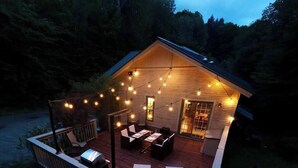 Una cabana de fusta acollidora amb terrassa, llums de garlandes i mobles d'exterior.