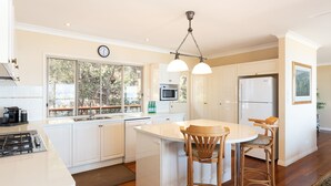 A modern kitchen with white cabinetry, a central island, a built-in microwave, and a refrigerator. - The Beachaus - Spacious Beachfront Holiday Home (Moreton Island)