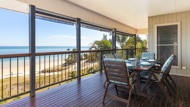 A balcony with a wooden floor, a table set for dining, and a view of the beach and ocean. - The Beachaus - Spacious Beachfront Holiday Home (Moreton Island)