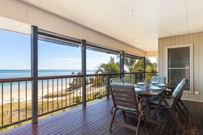 A balcony with a wooden floor, a table set for dining, and a view of the beach and ocean. - The Beachaus - Spacious Beachfront Holiday Home (Moreton Island)