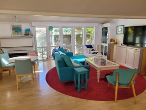 Un salón espacioso con alfombra roja, sofás color turquesa, sillas de madera y un piano.