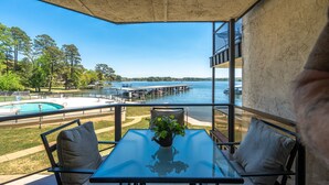 A balcony with a glass table, two chairs, and a potted plant. It overlooks a swimming pool and a marina with boats. - Exquisite Lakefront Condo - Pool - Boat Slip (Hot Springs)