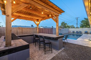 An outdoor patio with a wooden pergola, a pool, and seating areas. - Relaxing Mesa 4BR Home with 2 En Suite Bedrooms, Pool/BBQ (Mesa)