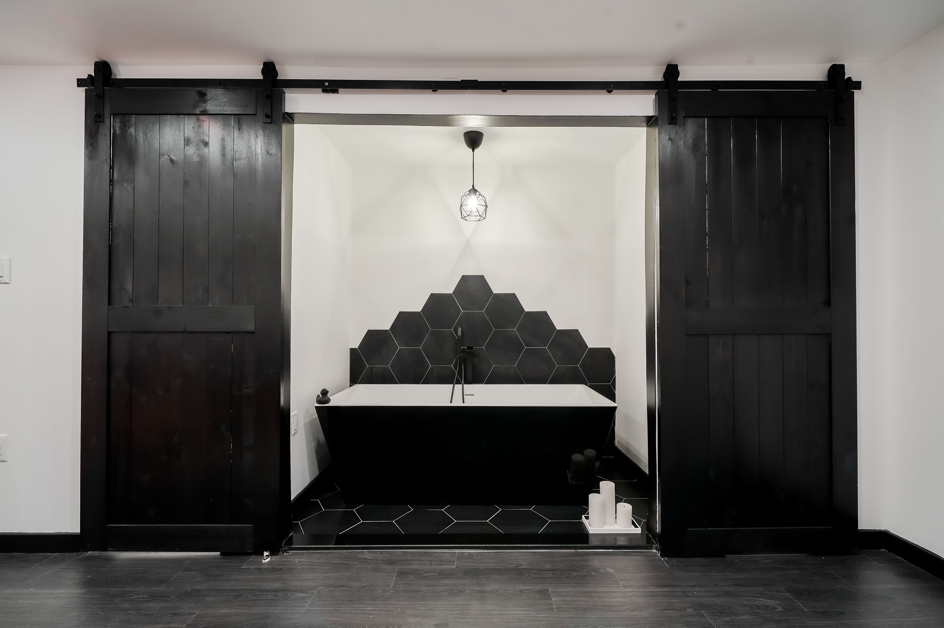 A modern bathroom with a black and white color scheme, featuring a large mirror, a black sink, and a hexagonal tile backsplash.