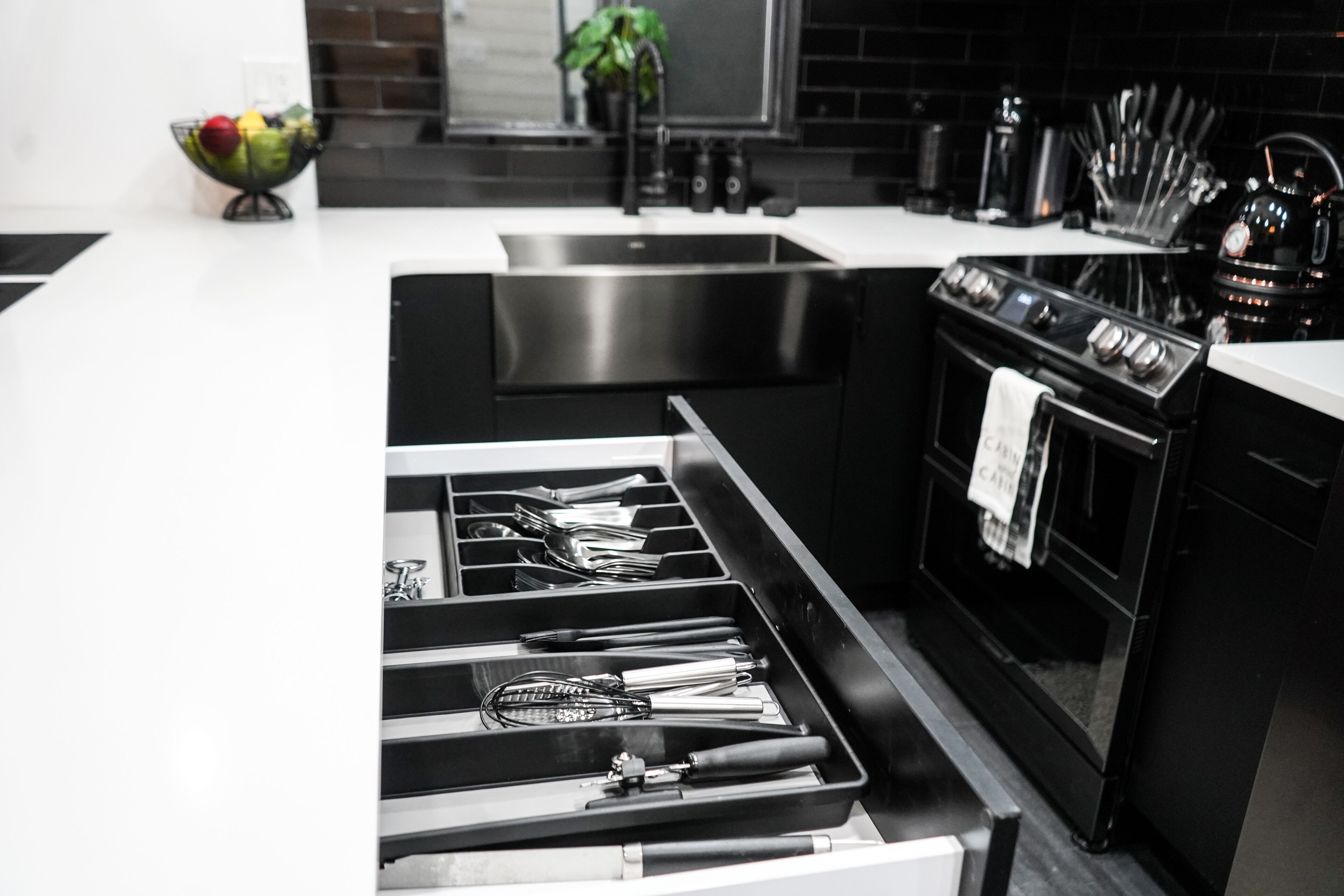 A modern kitchen with a stainless steel sink, black appliances, and a drawer organizer with utensils.