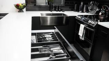 A modern kitchen with a stainless steel sink, black appliances, and a drawer organizer with utensils.