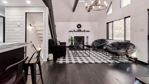 Un salon moderne avec une cheminée, un tapis à carreaux noir et blanc et un escalier menant à un niveau supérieur.