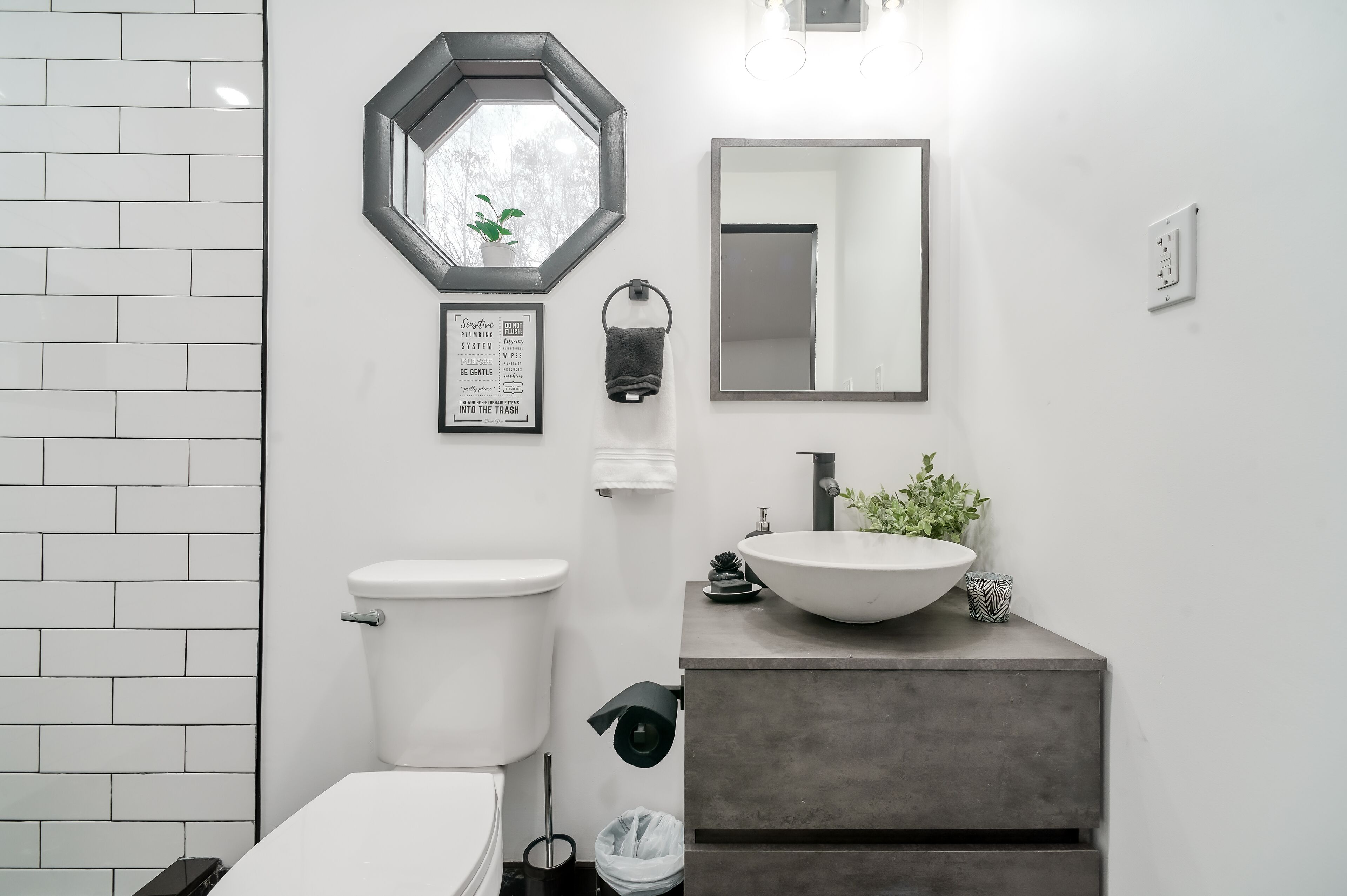 Ein modernes Badezimmer mit Toilette, einem großen Waschbecken mit Hohlkörperbecken, einem Spiegel und einem Schild über der Toilette.