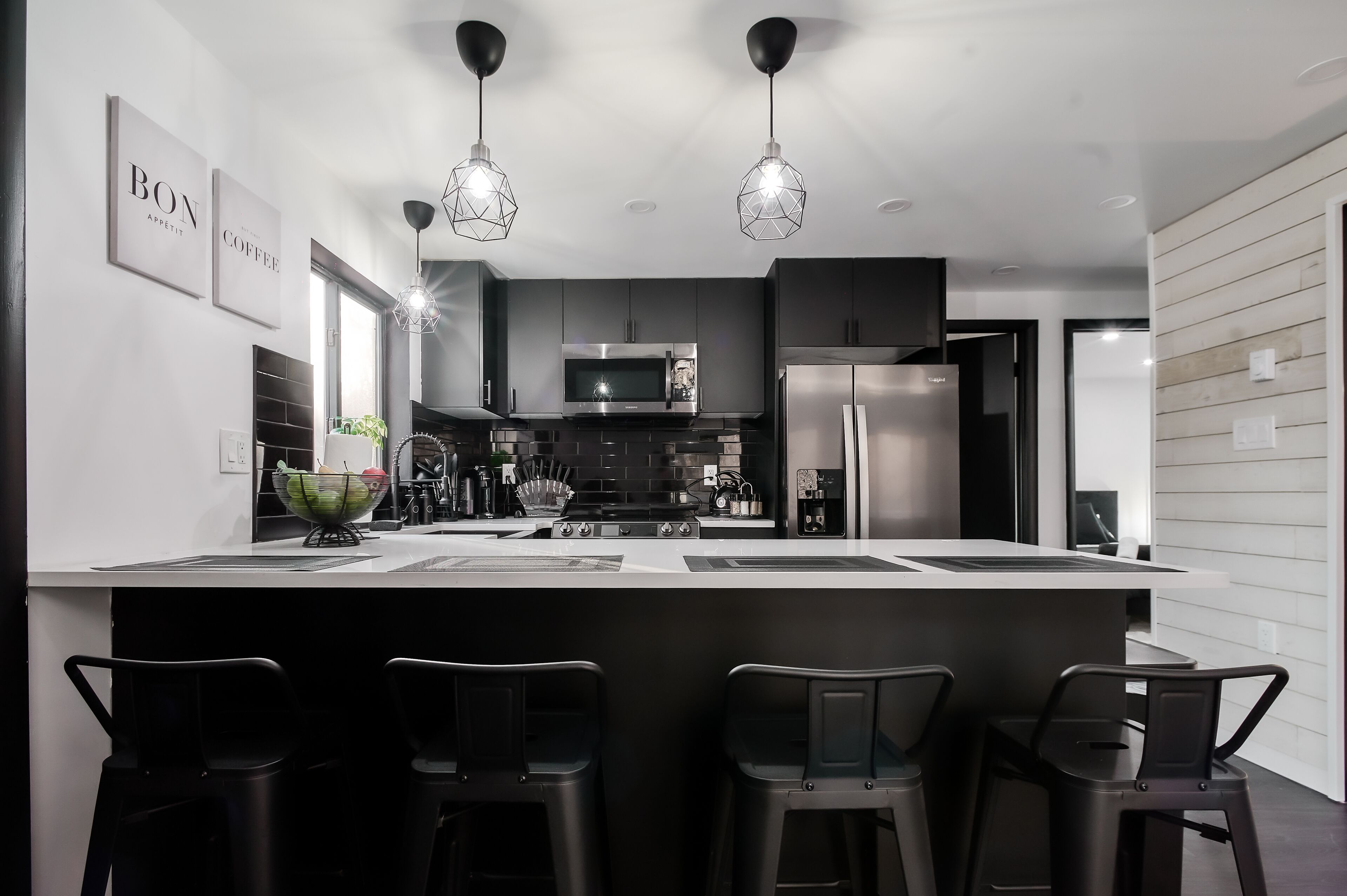 A modern kitchen with a central island, bar stools, stainless steel appliances, and pendant lighting.