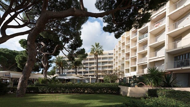 A multi-story hotel with balconies, surrounded by well-maintained greenery and palm trees. - Ref: SUP115: 2-room apartment in beachfront residence in Le Lavandou 4 pers (LE LAVANDOU)