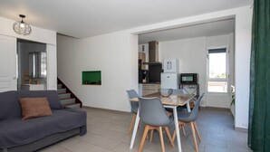 A modern living room with a sofa, dining table, and chairs. There is a staircase leading to another level, a kitchen with appliances, and a green wall decoration. - Ref: SUP115: 2-room apartment in beachfront residence in Le Lavandou 4 pers (LE LAVANDOU)