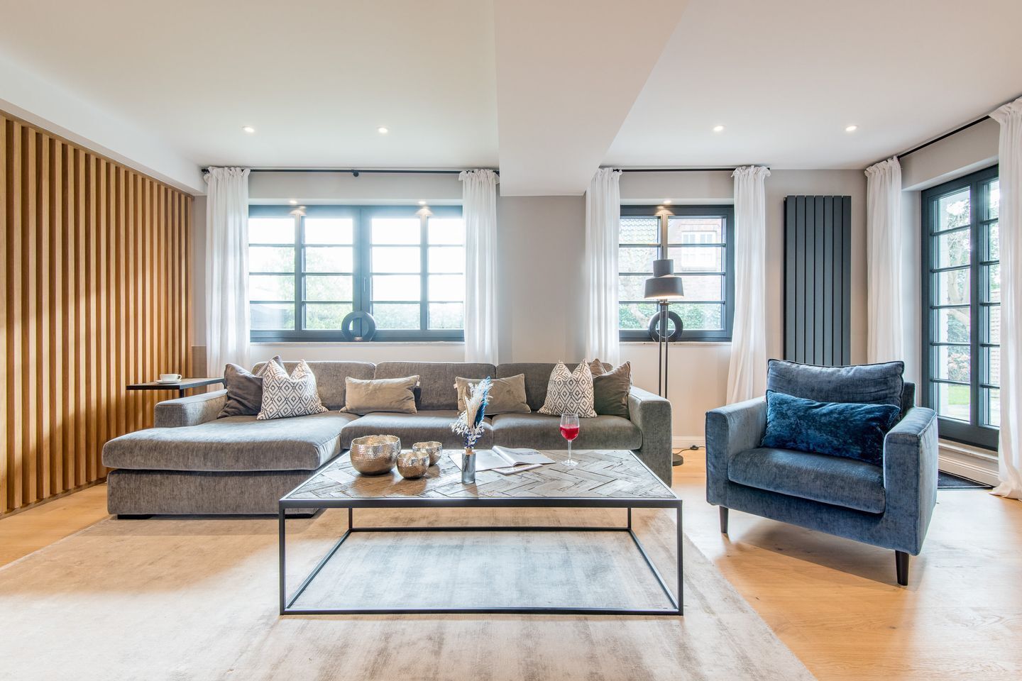 A modern living room with a grey sofa, a blue armchair, and a coffee table with decorative items.